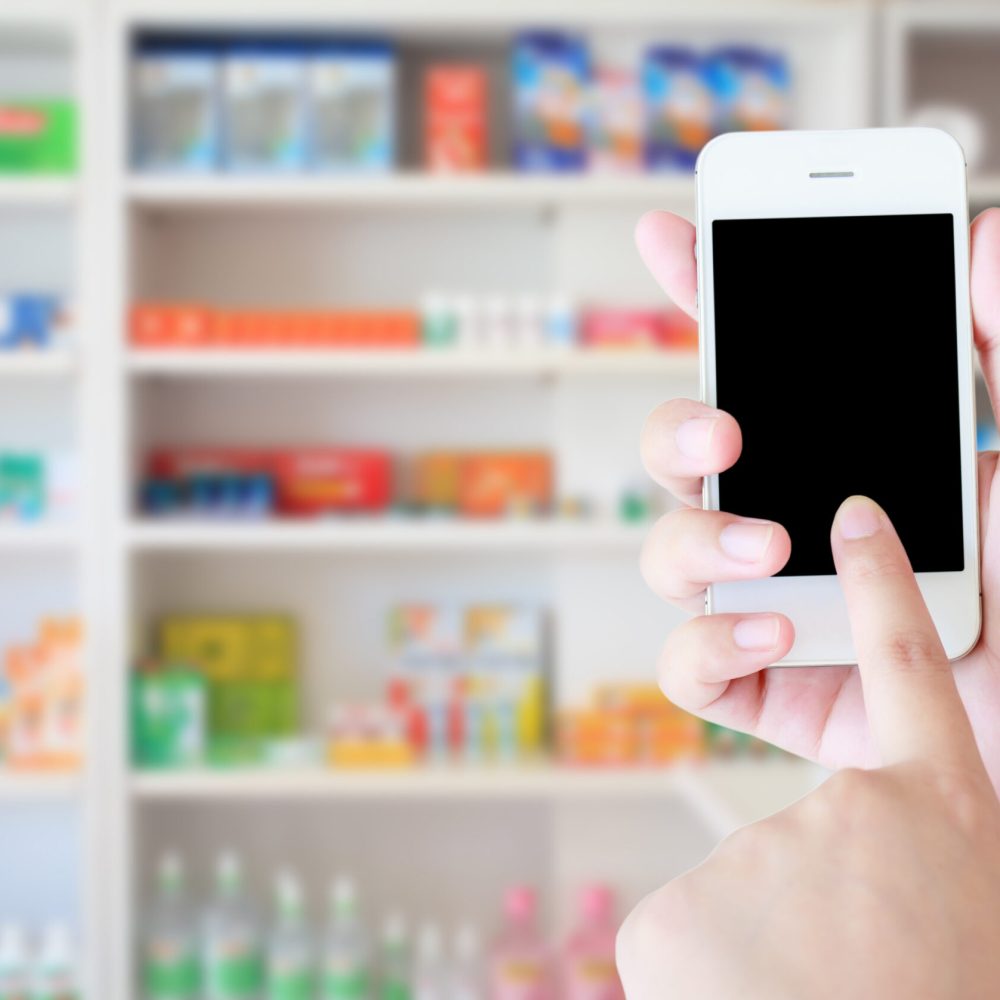 pharmacist hand holding smart phone with blur some shelves of drug in the pharmacy drugstore